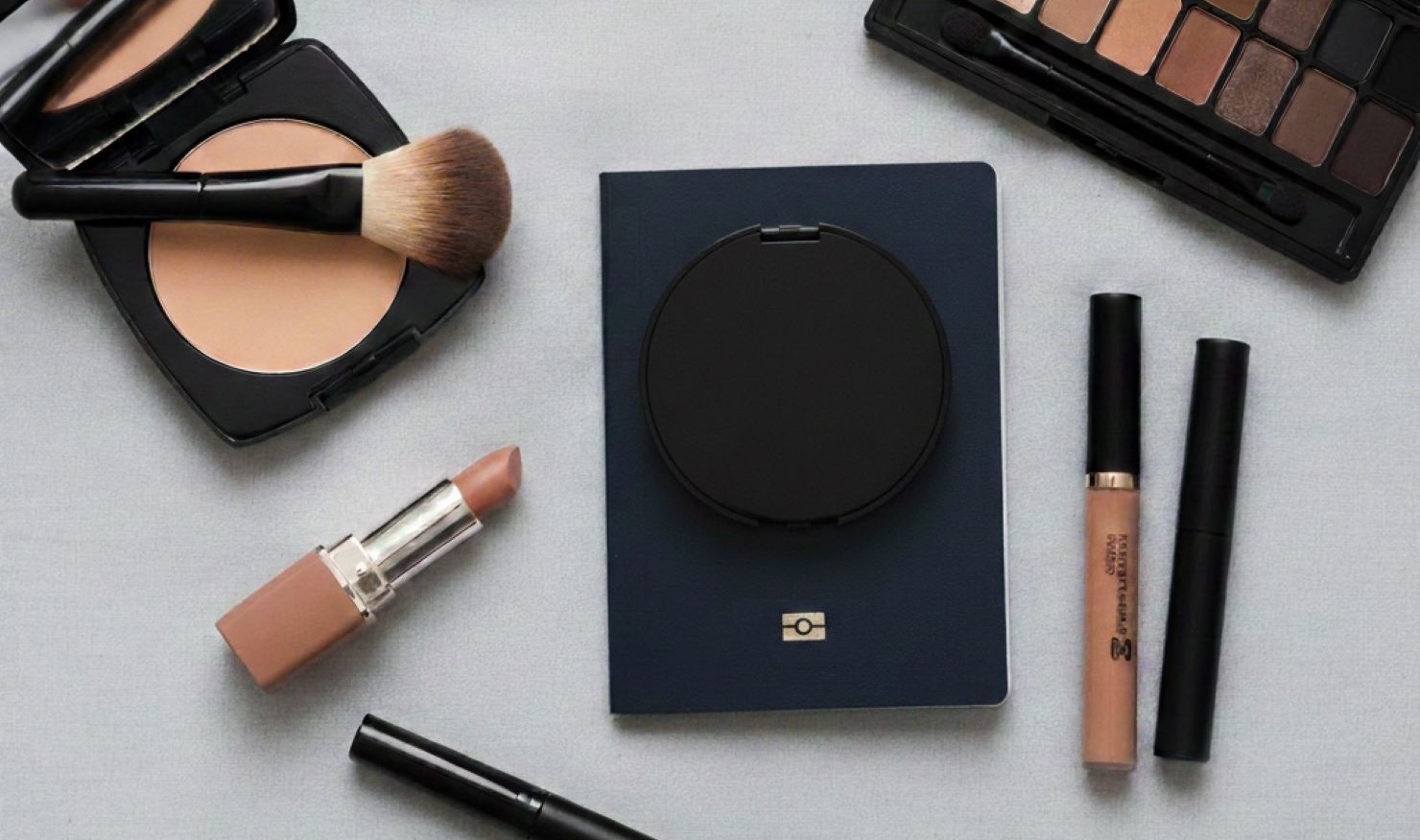 flat lay of a closed Australian passport with neutral makeup brushes, lipstick, and a matte powder palette
