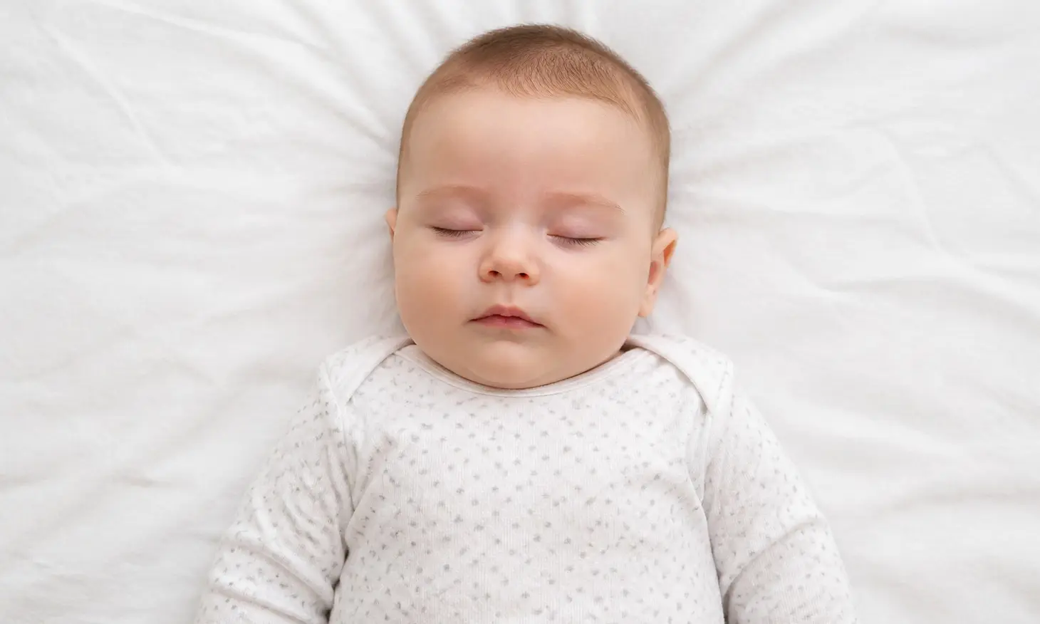 Overhead UK baby passport photo of an infant on a plain off-white sheet with even light and no adult hands in the frame